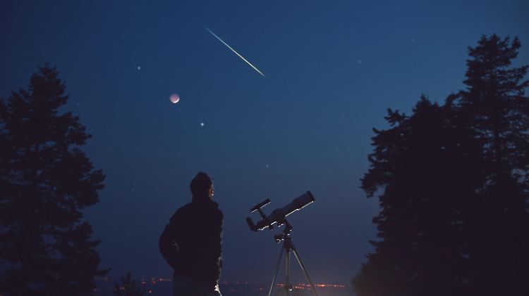 Silhouette of a man, telescope, stars, planets and shooting star under the night sky.