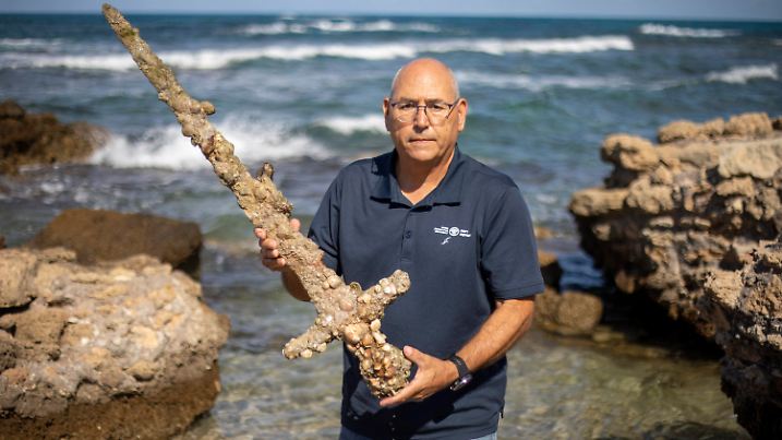 Jacob Sharvit, director of the Marine Archaeology Unit of the Israel Antiquities Authority holds a meter-long (yard-long) sword, that experts say dates back to the Crusaders is on display in Mediterranean seaport of Cesarea, Israel, Tuesday, Oct. 19, 2021. Israeli archaeologists say a scuba diver has salvaged an ancient sword off the country's Mediterranean coast that experts say dates back to the Crusaders. Israel's Antiquities Authority said Monday the man was on a weekend dive in northern Israel last Saturday when he spotted a trove of ancient artifacts that included anchors, pottery and a meter-long (yard-long) sword. Fearing the sword would be covered up by shifting sands, it says the man took it ashore and handed it over to government experts. Archaeologists believe that many ancient treasures are submerged in the area. The diver was given a certificate of appreciation for turning over the 900-year-old item. (AP Photo/Ariel Schalit)