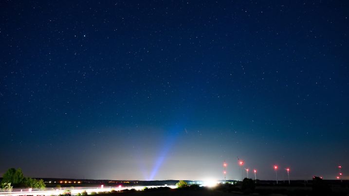 PRODUKTION - 06.05.2022, Brandenburg, Jacobsdorf: Hell erleuchtet ist die Autobahn A12, am Rand das rote Licht der Windenergieanlagen und im Hintergrund erhellt blaues Licht den Nachthimmel über der Stadt Frankfurt (Oder). Angestrahlte Kirchen und Denkmäler, Flutlicht im Stadien und grelle Straßenbeleuchtung - die Menschen machen vielerorts die Nacht zum Tag, mit verheerenden Folgen für die Tierwelt und die Artenvielfalt. (zu dpa-KORR.: "Schattenseite des Lichts: Lichtverschmutzung wird für Tiere zur Qual") Foto: Patrick Pleul/dpa +++ dpa-Bildfunk +++