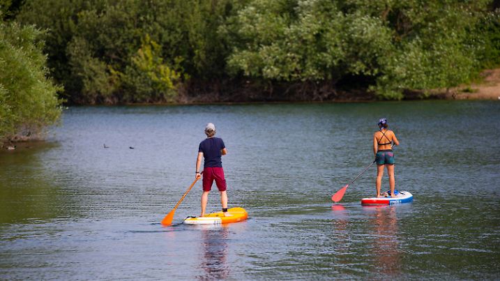 17.06.2022, Nordrhein-Westfalen, Köln: Zwei Stand-Up-Paddler gleiten über den Fühlinger See. Die Menschen in Nordrhein-Westfalen müssen sich in den nächsten Tagen auf Sonne und Hitze mit bis zu 37 Grad einstellen. Foto: Thomas Banneyer/dpa +++ dpa-Bildfunk +++