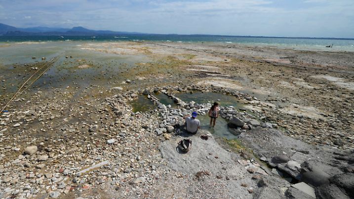 ARCHIV - 12.08.2022, Italien, Sirmione: ACHTUNG: DIESER BEITRAG DARF NICHT VOR DER SPERRFRIST, 18. Mai, 20 UHR, VERÖFFENTLICHT WERDEN! EIN BRUCH DES EMBARGOS KÖNNTE DIE BERICHTERSTATTUNG ÜBER STUDIEN EMPFINDLICH EINSCHRÄNKEN. Ein Mann sitzt neben einem Kind am Gardasee. Der Wasserstand des Gardasees war damals nach einer schweren Dürre stark gesunken, wodurch die Steine, die die Halbinsel von Sirmione umgeben, freigelegt wurden. (Zu dpa "Studie: Über die Hälfte der weltweit größten Seen verliert Wasser") Foto: Antonio Calanni/AP/dpa +++ dpa-Bildfunk +++
