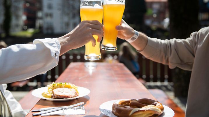 ARCHIV - 28.03.2021, Baden-Württemberg, Tübingen: Zwei Menschen sitzen bei gutem Wetter in einem Biergarten und stoßen mit einem Bier an.Der Regenschirm kann dieses Wochenende im Schrank bleiben, doch die Sonnencreme ist bei Ausflügen oder beim Baden ein Muss. (zu dpa: «Sonne satt - Meteorologen erwarten schöne Pfingsten im Südwesten»). Foto: Tom Weller/dpa +++ dpa-Bildfunk +++