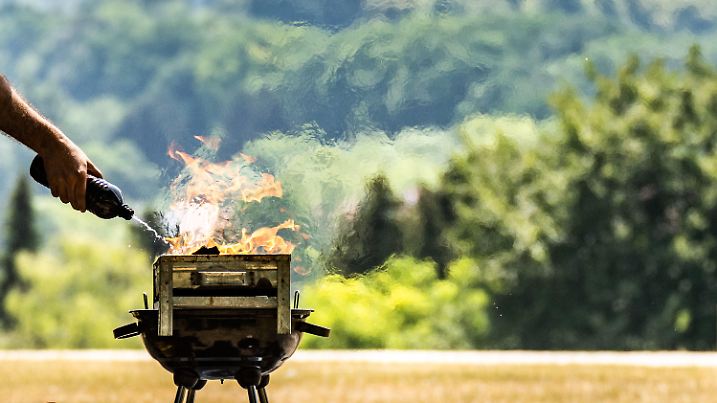 19.06.2022, Hessen, Frankfurt/Main: Ein Mann spritzt Brennspritus aus einer Flasche, um in der Nachmittagshitze das Feuer in einem Grill auf dem Lohrberg mit Blick auf die Skjyline der Stadt anzuheizen. Im Süden Hessens wurden bis zu 37 Grad Hitze gemeldet und wegen der Trockenheit mangels Niederschlägen besteht in Teilen des Landes weiter hohe Waldbrandgefahr. Foto: Frank Rumpenhorst/dpa +++ dpa-Bildfunk +++