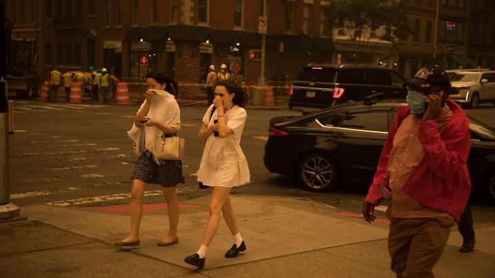 07.06.2023, USA, New York: Fußgänger, die ihr Gesicht bedecken, gehen an einer Straße entlang. Der Rauch zahlreicher schwerer Waldbrände in Kanada hat Teile der US-Ostküste eingehüllt und in der Millionenmetropole New York für die schlechteste Luftqualität seit Jahrzehnten gesorgt. Die Schwaden Hunderter Feuer im Osten Kanadas zogen in südliche Richtung und führten unter anderem in New York zu einem dichten, nebligen Schleier und einer zeitweise orangenen Färbung des Himmels. Foto: Michael Nagel/XinHua/dpa +++ dpa-Bildfunk +++