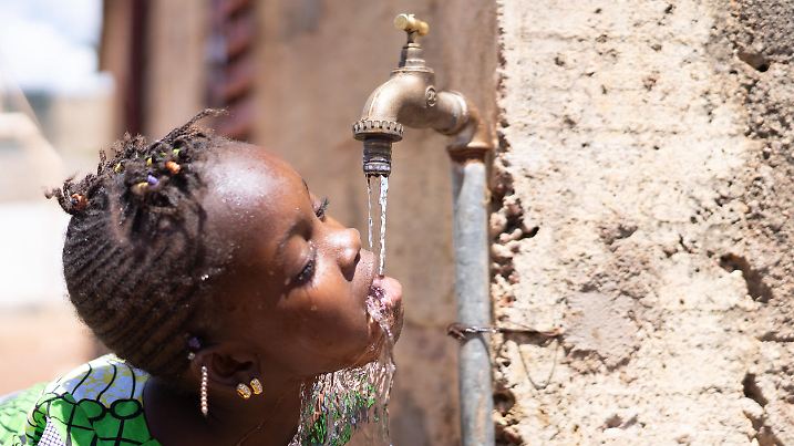 Joyful Black Child Drinks Fresh Water from a Tap. Candid Picture of African children drinking and playing with water in Bamako, Mali.