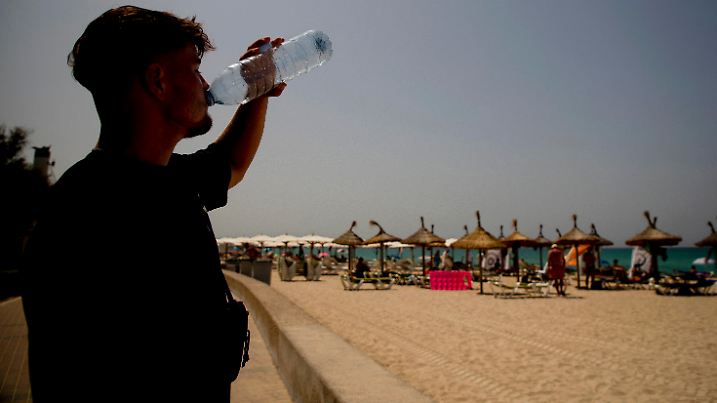 18.07.2023, Spanien, Palma de Mallorca: Etienne aus Biberach trinkt bei heißen Temperaturen am Strand von Arenal Wasser. Für den Norden und Osten der spanischen Mittelmeer-Insel Mallorca kündigte der nationale Wetterdienst Aemet Höchsttemperaturen von mindestens 43 Grad an. Der Höhepunkt der dritten Hitzewelle des Sommers in Spanien bringt Einheimische und Touristen im beliebten Urlaubsland ins Schwitzen. Foto: Clara Margais/dpa +++ dpa-Bildfunk +++