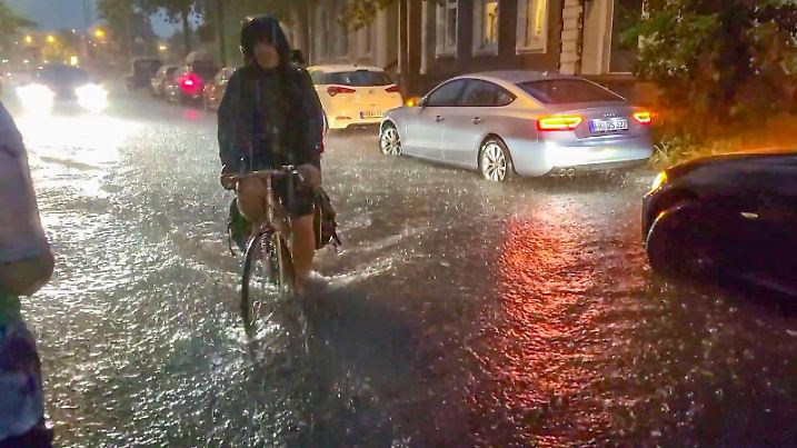 24.08.2023, Baden-Württemberg, Freiburg im Breisgau: Ein Fahrradfahrer fährt über eine vom Regen überschwemmte Straße. Der Deutsche Wetterdienst (DWD) hat für Donnerstagabend vor Unwettern in Stuttgart, Tübingen und Freiburg gewarnt. Es könne es zu schweren Gewittern kommen, teilte der DWD mit. Foto: -/Einsatz-Report24 /dpa +++ dpa-Bildfunk +++
