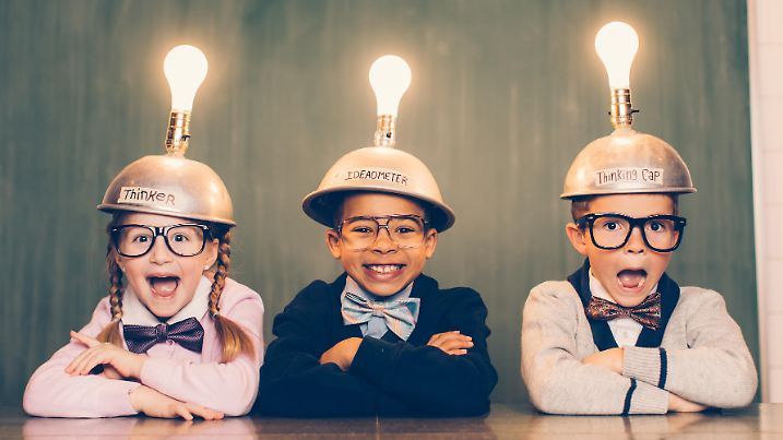 Three young nerds sit in a classroom setting with a thinking cap on their heads. They are suprised and smiling as their light bulbs are lit as the new ideas are flowing. They're wearing cardigans and bow ties. Learning is fun when you have ideas.