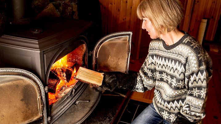 Eine Frau legt ein Stück Holz in den Kaminofen.