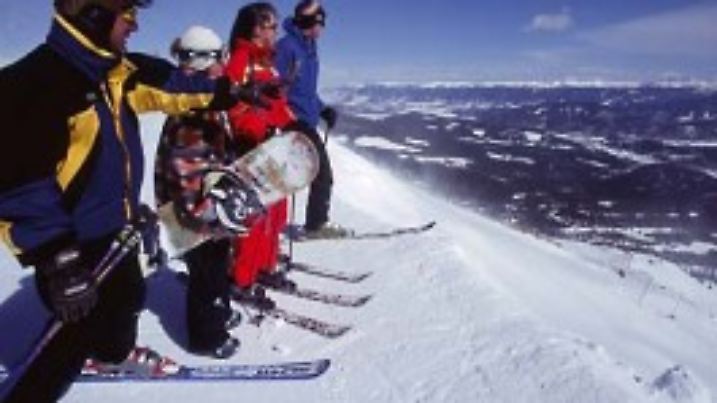 Familie mit zwei Kindern steht vor Skiabfahrt an Hangkante.