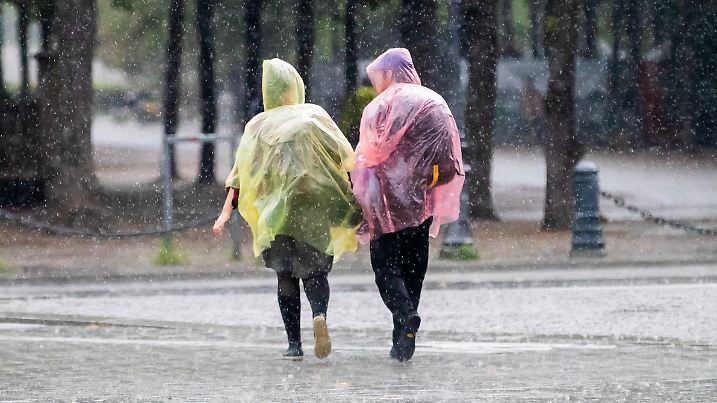 26.08.2022, Berlin: Passanten mit Plastik-Regenschutz gehen nahe des Brandenburger Tors durch den Regen. Foto: Christoph Soeder/dpa +++ dpa-Bildfunk +++