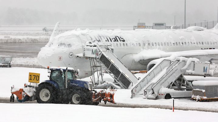 02.12.2023, Bayern, München: Ein Räum- und Streufahrzeug fährt im Schneetreiben auf dem Flughafen an einer verschneiten Maschine von Lufthansa vorbei. Die Sperrung des Flugbetriebes am Münchner Flughafen ist wegen starker Schneefälle bis 03.12.2023 um 6.00 Uhr verlängert worden. Foto: Karl-Josef Hildenbrand/dpa +++ dpa-Bildfunk +++