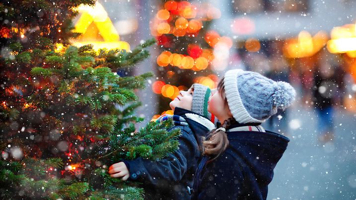 Two little kids, boy and girl having fun on traditional Christmas market during strong snowfall. Happy children enjoying traditional family market in Germany. Twins standing by illuminated xmas tree
