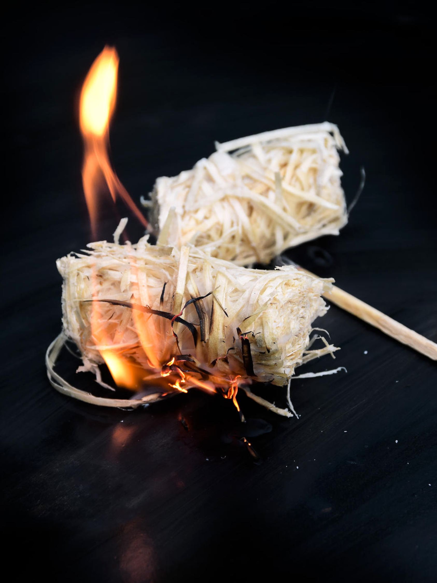 burning wood wool barbecue lighter on a black metal bowl, copy space, selected focus