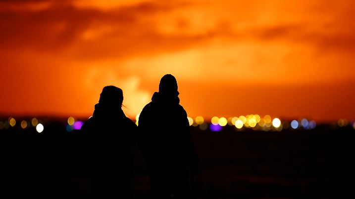 18.12.2023, Island, Reykjavik: Menschen beobachten, wie der Nachthimmel nach dem Ausbruch eines Vulkans auf der Halbinsel Reykjanes im Südwesten Islands von der Hauptstadt Reykjavik aus gesehen erhellt wird. Auf der Reykjanes-Halbinsel in Island ist am späten Montagabend ein Vulkan ausgebrochen. Das teilte das isländische Wetteramt mit. Foto: Brynjar Gunnarsson/AP +++ dpa-Bildfunk +++