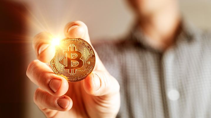 Kryptowährung goldene leuchtende Bitcoin Münze in der Hand eines Mannes Symbol der Kryptowährung elektronisches virtuelles Geld FOTOMONTAGE