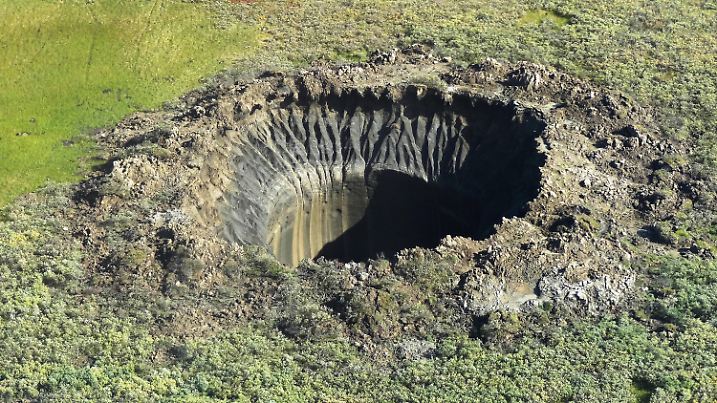 An aerial view from onboard a helicopter taken on August 25, 2014 shows a crater on the Yamal Peninsula, northern Siberia. Russian scientists have now discovered seven giant craters in remote Siberia, the deputy director of the Oil and Gas Research Institute of the Russian Academy of Sciences, Vasily Bogoyavlensky, told AFP on March 12, adding that the mysterious phenomenon was believed to be linked to climate change.  (Photo by VASILY BOGOYAVLENSKY/AFP via Getty Images)