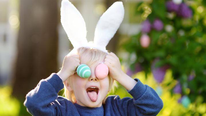 Little child wearing bunny ears playing with eggs in spring park on Easter day. Traditional easter festival outdoors.