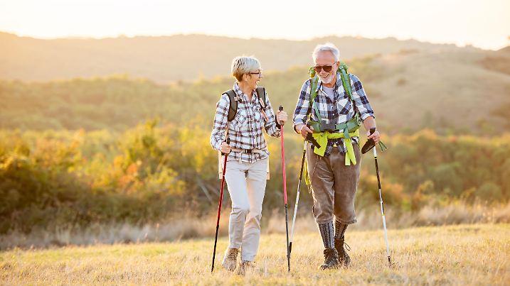 Active senior Caucasian couple hiking in mountains with backpacks and hiking poles, enjoying their adventure