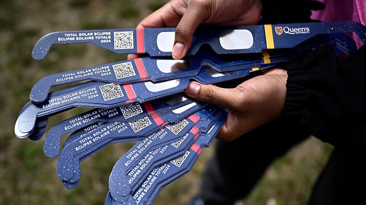 A volunteer shows solar eclipse glasses being given away as part of a Queen's University outreach program, before the start of a total solar eclipse, in Kingston, Ontario, Monday, April 8, 2024. (Justin Tang/The Canadian Press via AP)