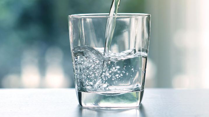 Close up pouring purified fresh drink water from the bottle on table in living room