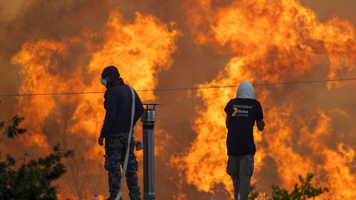 dpatopbilder - 25.07.2023, Griechenland, Gennadi: Gegen Abend erreichen Flammen die Ortschaft Gennadi, Anwohner stehen auf ihren Dächern vor riesigen Flammen und versuchen mit Wasserschläuchen ihre Häuser zu retten. Hitze am Mittelmeer - Tausende Menschen fliehen vor Waldbränden auf Rhodos. In Griechenland toben Waldbrände in zahlreichen Regionen. Betroffen sind auch beliebte Ferienorte wie die Inseln Rhodos und Korfu. Foto: Christoph Reichwein/dpa +++ dpa-Bildfunk +++