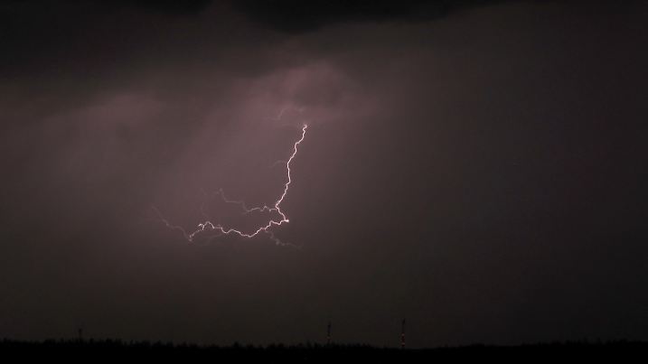 Ein Blitz entlädt sich am Himmel über dem nächtlichen Alpenvorland.