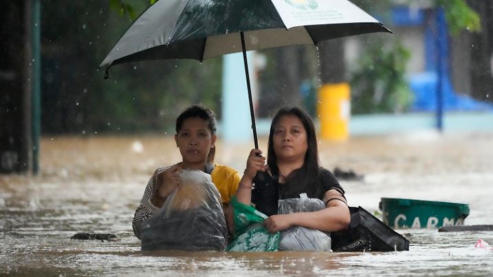 Residents protect their belongings as they negotiate a flooded street caused by heavy rains from Tropical Storm Yagi, locally called Enteng, in Cainta, Rizal province, Philippines, Monday, Sept. 2, 2024. (AP Photo/Aaron Favila)