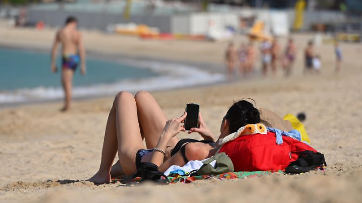 Schlanke Frau im Bikini liegt alleine,einsam am Strand Le Mer in Dubai und blickt auf ihr Smartphone,Handy am 02.01.2023. ?