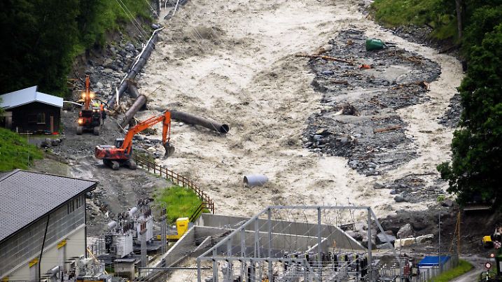 21.06.2024, Schweiz, Vissoie: Bagger arbeiten im Val d'Anniviers am Ufer des Hochwasser führenden Flusses Navisence in der Nähe des Alpiq-Wasserkraftwerks. In den Schweizer Kantons Graubünden und Wallis gab es seit Freitag zahlreiche Gewitter und heftige Niederschläge, Hochwasser und einen Bergsturz. Foto: Jean-Christophe Bott/KEYSTONE/dpa +++ dpa-Bildfunk +++
