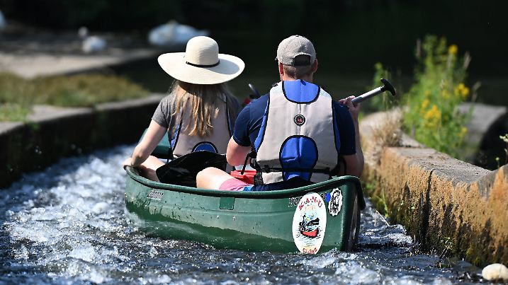 ARCHIV - 09.07.2023, Hessen, Gießen: Ein Pärchen steuert bei einem Ausflug auf dem Wasser ein Kanu durch eine Bootsgasse an einem Wehr der Lahn. (zu dpa: «Trotz Schmuddelwetters: Freizeiteinrichtungen sind zufrieden») Foto: Arne Dedert/dpa +++ dpa-Bildfunk +++