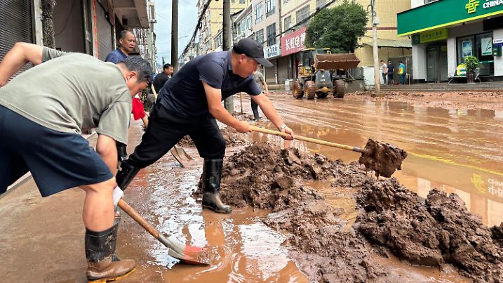 23.06.2024, China, Huaihua: Dieses mit einem Mobiltelefon aufgenommene Foto zeigt Menschen, die eine Straße in der Gemeinde Wuqiangxi im Kreis Yuanling in der zentralchinesischen Provinz Hunan vom Schlamm befreien. Schwere Regenfälle trafen die Gemeinde Wuqiangxi am Samstag und führten zu Überschwemmungen, die auch Wohngebiete in Mitleidenschaft zogen. Die örtlichen Behörden haben Notfallmaßnahmen ergriffen, um die Auswirkungen der extremen Wetterbedingungen zu minimieren. Foto: Yu Chunsheng/XinHua/dpa +++ dpa-Bildfunk +++
