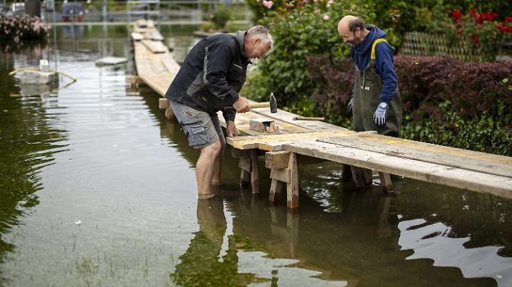 11.06.2024, Schweiz, Berlingen: Ein Gemeindeangestellter und ein Freiwilliger bauen Stege, während der Untersee, der westliche Teil des Bodensees, über die Ufer tritt. Der Bund hat am Dienstag für den westlichen Teil des Bodensees die höchste Gefahrenstufe ausgerufen. An mehreren Stellen stehen Uferpromenaden, Parkplätze und Gartenrestaurants unter Wasser. Mit mobilen Deichanlagen und Sandsäcken wird versucht, das Wasser aus dem See zurückzuhalten. Foto: Michael Buholzer/KEYSTONE/dpa +++ dpa-Bildfunk +++