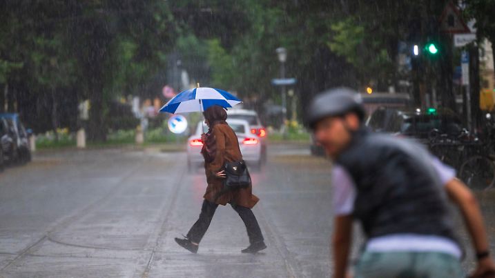 26.06.2024, Bayern, München: Eine Frau mit einem Regenschirm geht bei starkem Regen über eine Strasse im Stadtteil Haidhausen. Foto: Peter Kneffel/dpa +++ dpa-Bildfunk +++