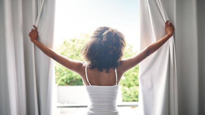Rearview of a young woman opening the curtains in her bedroom