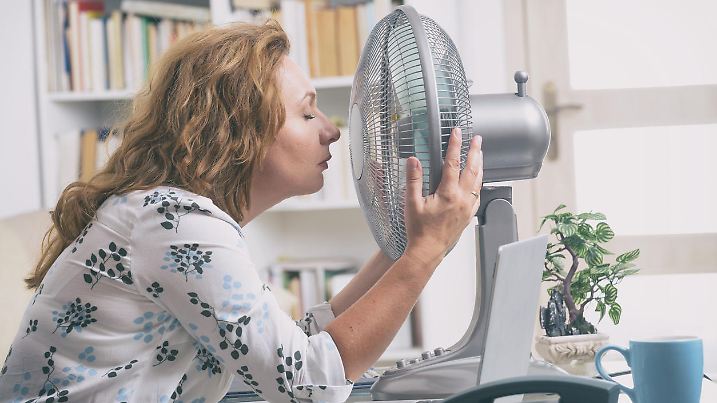 Woman suffers from heat while working in the office and tries to cool off by the fan