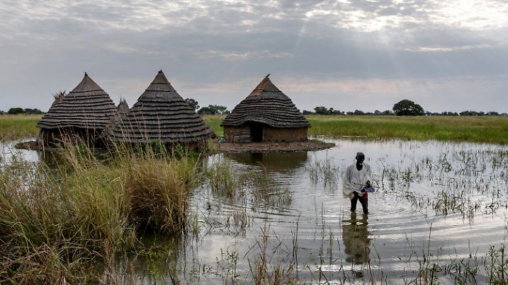 ARCHIV - 20.10.2021, Südsudan, Malualkon: Ein Mann watet durch das Hochwasser auf seinem Grundstück in einem südsudanesischen Dorf. Nachdem der Südsudan bereits 2021 schwere Überschwemmungen in der Regenzeit erlitt, werden in der nun einsetzenden Regenzeit die schwersten Fluten seit Jahrzehnten erwartet. (zu dpa: «Fast 90 Schlangenangriffe nach Regenfällen im Südsudan») Foto: Adrienne Surprenant/AP/dpa +++ dpa-Bildfunk +++