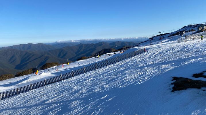 An aerial view of a snow-covered ski slope in Australia, with the sun glistening off of the white powdery snow Model Released Property Released xkwx aerial alpine alps australia beauty bright cold downhill fresh glacial glisten landscape majestic mountains nature outdoor peaceful picturesque powder powdery resort scenic serene ski slope snow snowfall snowy summit sun tranquility view vista white winter