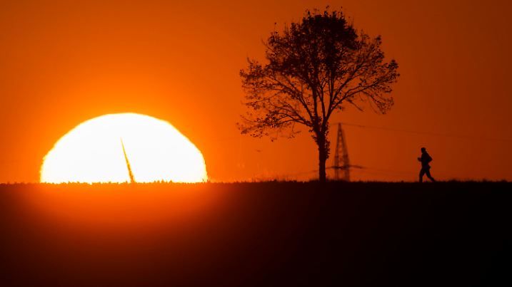 21.09.2020, Niedersachsen, Algermissen: Eine Frau joggt am frühen Morgen beim Sonnenaufgang über einen Feldweg im Landkreis Hildesheim. In der Sonne ist zudem ein Rotorblatt eines Windrades zu erkennen. Foto: Julian Stratenschulte/dpa +++ dpa-Bildfunk +++