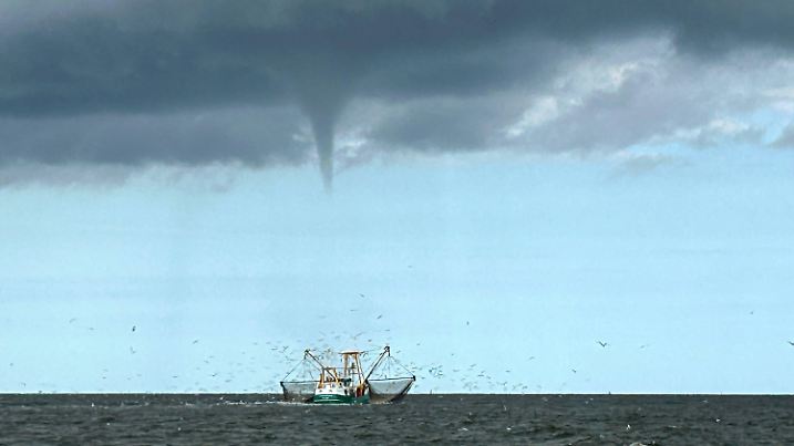 08.08.2024, Niedersachsen, Borkum: Das von einem Fischerboot aufgenommene Foto zeigt einen entstehenden mutmaßlichen Tornado vor der Nordseeinsel Borkum und ein Fischerboot. Ein mutmaßlicher Tornado hat am Strand der Nordseeinsel Borkum für kleinere Verwüstungen gesorgt. Der Wirbelsturm zog am Donnerstag vom Meer her über einen Abschnitt des Weststrandes und weiter zur Promenade, wie auf Videos im Internet zu sehen war. Foto: Rolf Groenewold/dpa +++ dpa-Bildfunk +++