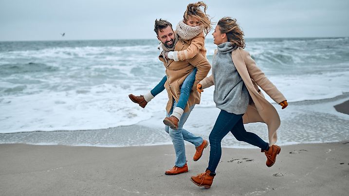 Portrait of a young married couple and their cute daughter who have fun on the beach in winter.
