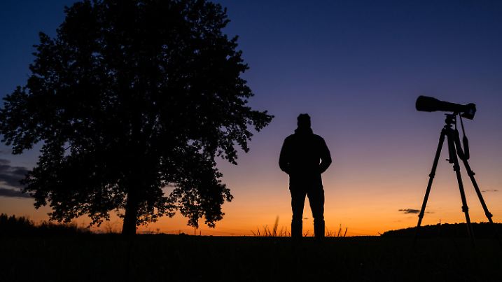 dpatopbilder - 11.10.2024, Brandenburg, Petersdorf: Ein Fotograf steht nach dem Sonnenuntergang mit seiner Ausrüstung auf einem Feld und wartet auf den Kometen Tsuchinshan-Atlas (Aufnahme mit Selbstauslöser). Voraussichtlich ab Freitagabend wird für mehrere Tage der vorbeiziehende Komet Tsuchinshan-Atlas - auch C/2023 A3 genannt - samt Schweif am Himmel zu beobachten sein. Foto: Patrick Pleul/dpa +++ dpa-Bildfunk +++
