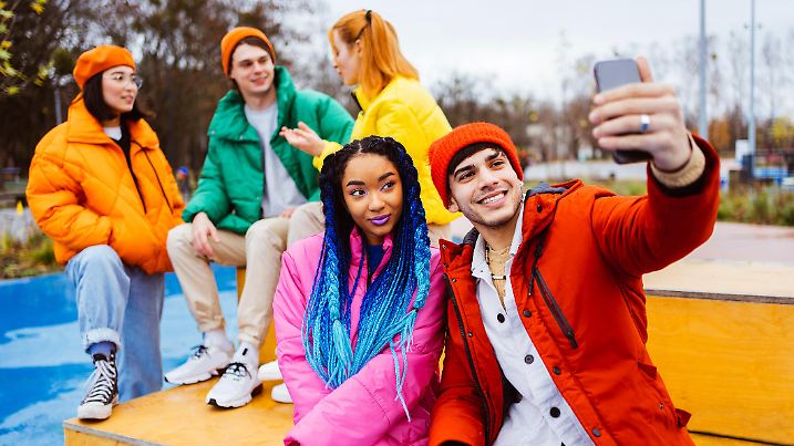 Multiracial group of young happy friends meeting outdoors in winter, wearing winter jackets and having fun, couple taking selfie on smartphone for social media - Multiethnic millennials bonding in a urban area, concepts about youth and social releationships
