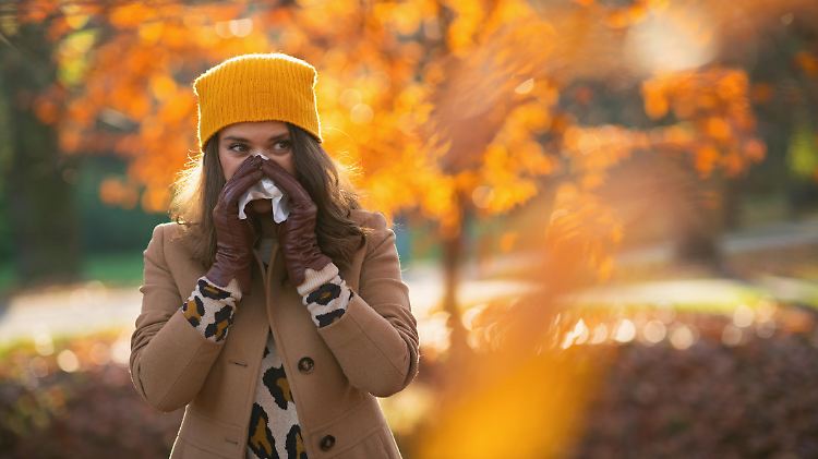 Hello autumn. modern 40 years old woman in brown coat and yellow hat with napkin blowing nose outdoors in the city park in autumn.