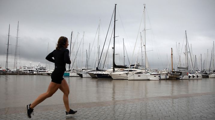 26.10.2024, Spanien, Palma de Mallorca: Eine Frau läuft an einem regnerischen Tag an der Hafenpromenade der Inselhauptstadt entlang. Regen und Stürme lassen die Temperaturen auf Mallorca sinken. Foto: Clara Margais/dpa +++ dpa-Bildfunk +++