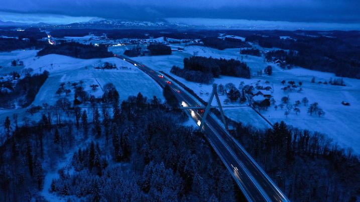 07.12.2021, Baden-Württemberg, Neuravensburg: Autos und Laster fahren auf der Autobahn 96 über eine Hängebrücke, die bei Neuravensburg über eine Schlucht führt. Im Hintergrund sind die Schweizer Alpen und stellenweise der Bodensee zu sehen. Über Nacht hat es im Allgäu geschneit. Aufnahme mit Drohne und Langzeitbelichtung Foto: Felix Kästle/dpa +++ dpa-Bildfunk +++