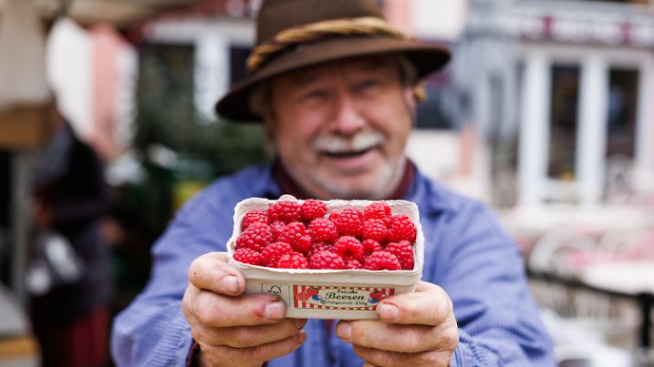 PRODUKTION - 12.11.2024, Baden-Württemberg, Freiburg: Obsthändler Walter Schwaab steht auf dem Freiburger Münsterplaz und hält eine Schale frischer Himbeeren aus der Region in den Händen. Trotz Herbstwetter mit einstelligen Temperaturen, Nebel und Wind wachsen in der Region Freiburg, die auch "Toskana Deutschlands" genannt wird, noch Himbeeren. Die roten Früchte verbinden viele mit dem Sommer - doch in Südbaden scheinen sie kurz vor dem Winter immer noch ein Renner zu sein. Die Himbeeren werden nicht in einem Gewächshaus angebaut. (zu dpa: «Rarität: Immer noch regionale Himbeeren auf dem Markt») Foto: Philipp von Ditfurth/dpa +++ dpa-Bildfunk +++