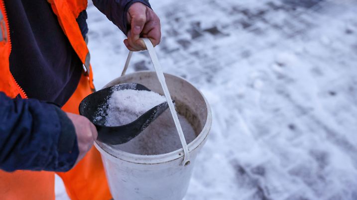 05.12.2023, Sachsen, Leipzig: Ein Mitarbeiter des Winterdienstes verteilt Streusalz bei Regen und Schneeglätte auf den Fußweg an einer Straßenkreuzung. Es soll auch in den kommenden Tagen weiter schneien oder regnen, die Temperaturen liegen bei null bis plus vier Grad. Der Deutsche Wetterdienst (DWD) warnt vor Glatteis durch überfrierenden Regen. Foto: Jan Woitas/dpa +++ dpa-Bildfunk +++