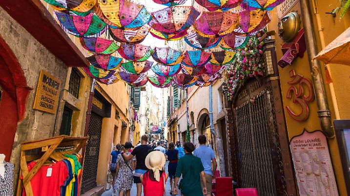 In der Altstadt von Nizza. In einer belebten Gasse hängen bunte Regenschirme/Sonnenschirme zwischen den Häusern.