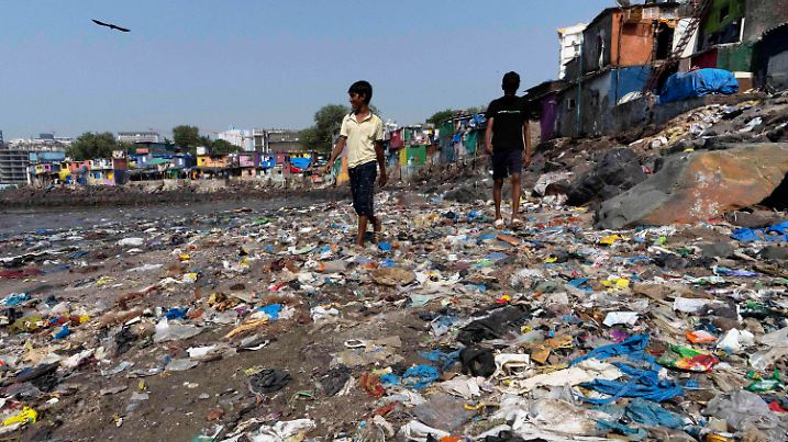 26.11.2024, Indien, Mumbai: Menschen spazieren am Strand des Badhwar Park an der Küste des Arabischen Meeres an Plastikmüll vorbei. Foto: Rajanish Kakade/AP/dpa +++ dpa-Bildfunk +++